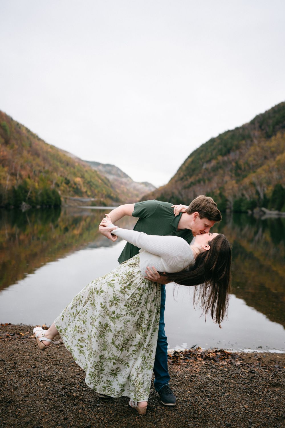 A romantic dip pose captured by a mountain lake during autumn with fall colors reflecting in the water.