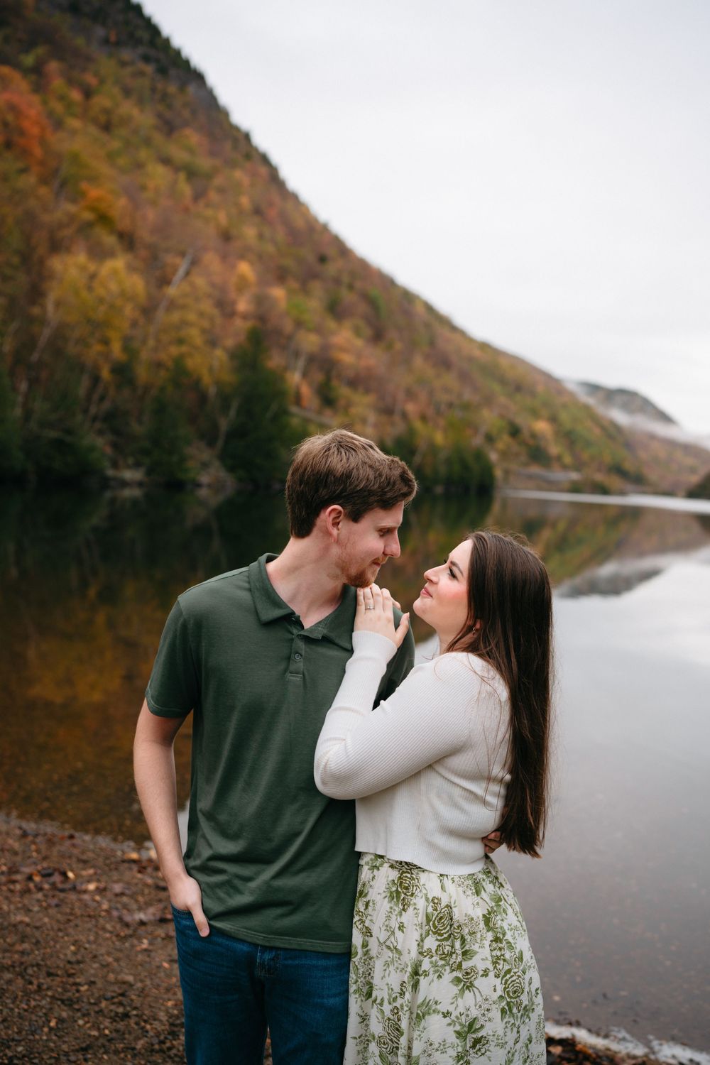 Sweet couple poses together near a peaceful mountain lake surrounded by autumn colors and natural beauty.