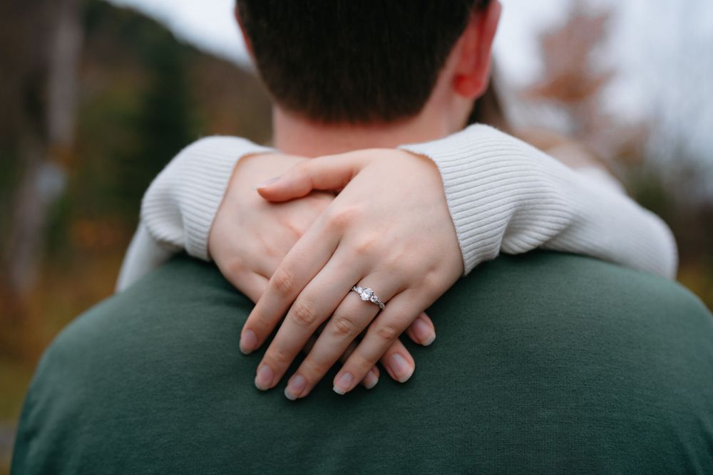 A close-up detail of hands embracing on a green sweater showing an engagement ring.