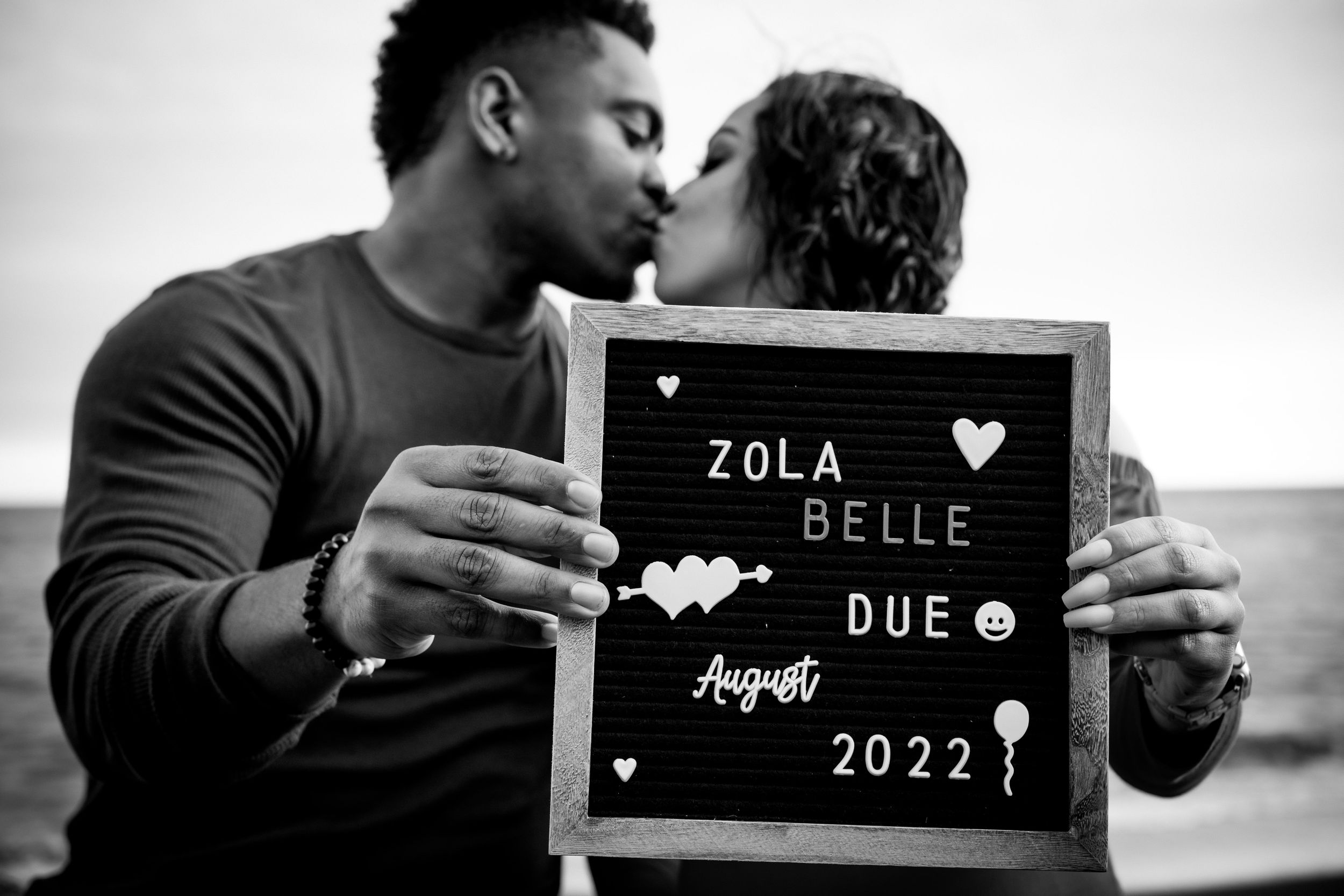 A series of black and white romantic engagement photos with couples holding letter boards and embracing.