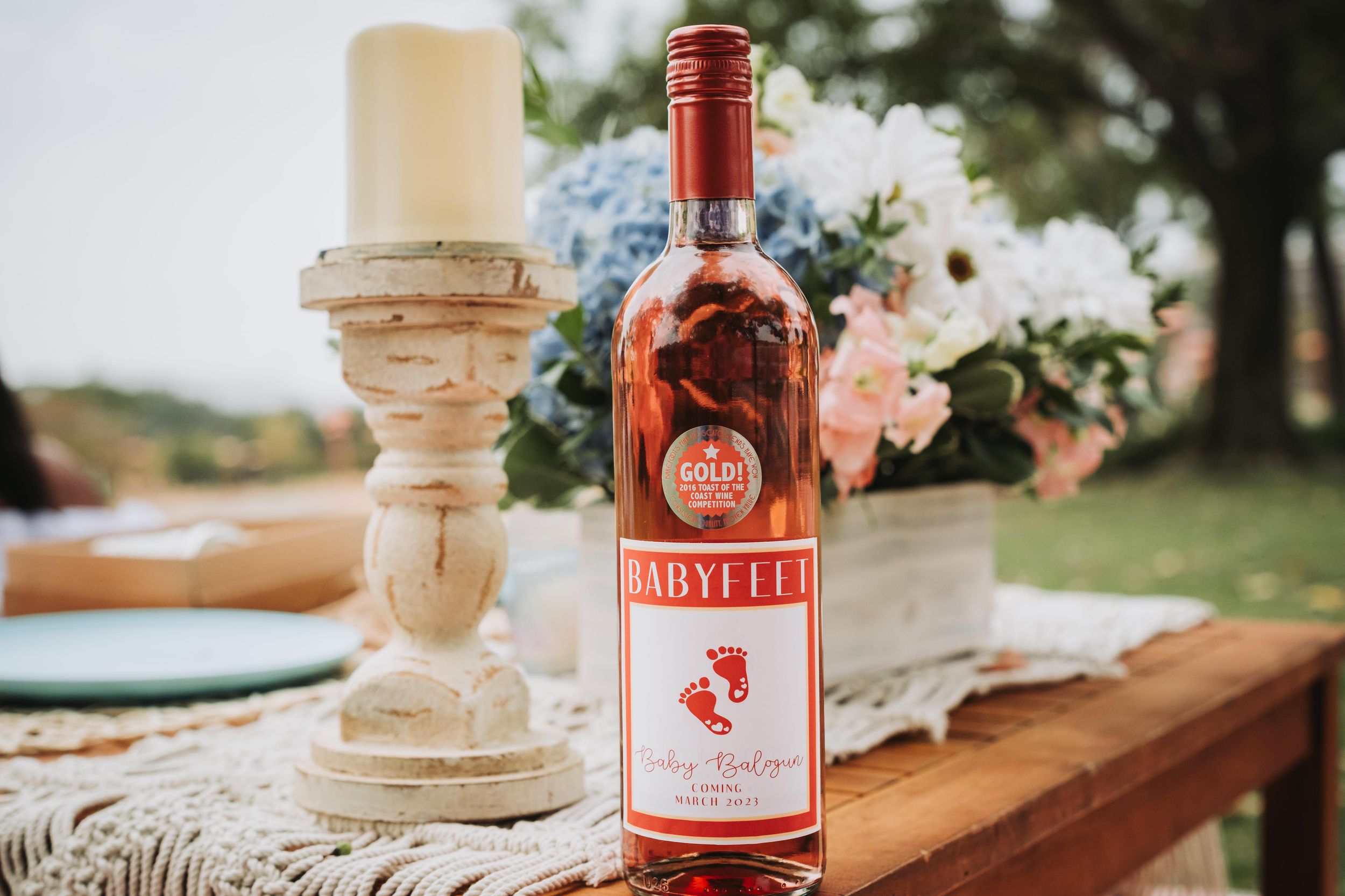 Rustic wooden table with wine bottles and elegant candle holders at an outdoor wedding reception setup.