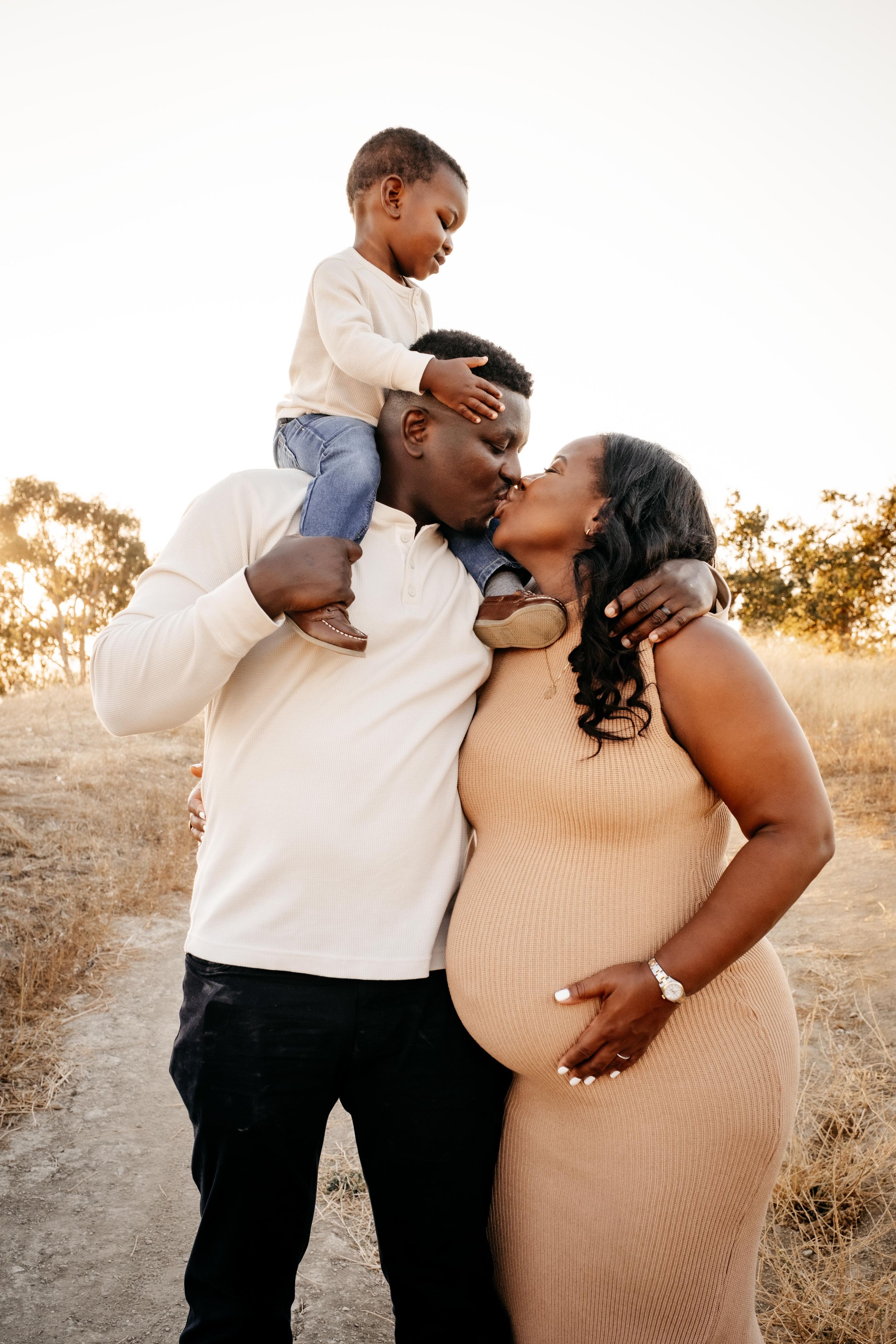 A loving family shares tender moments during a golden hour maternity photoshoot in a rustic outdoor setting.