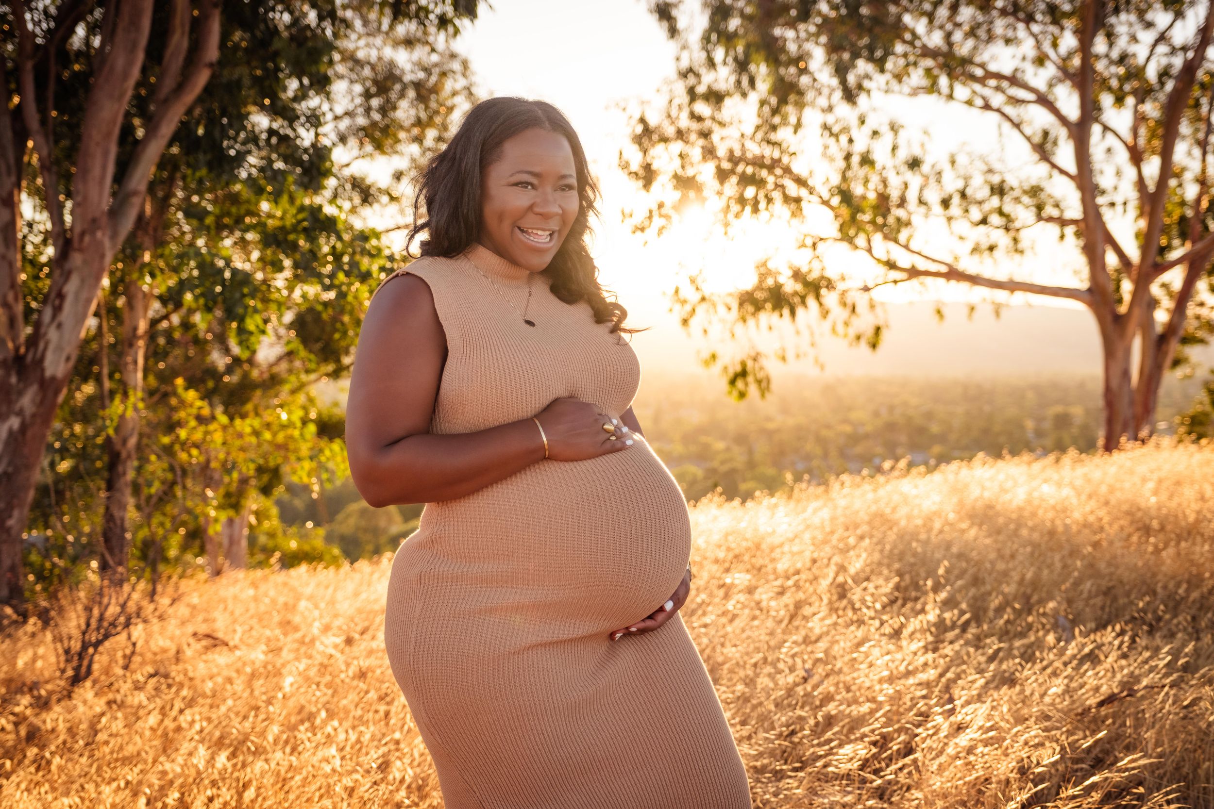 Maternity photoshoot at sunset in a golden field with tall grass and eucalyptus trees in the background.