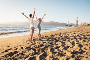 Couple with arms raised on Baker Beach with Golden Gate Bridge backdrop in San Francisco.