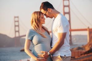 Pregnant couple embracing near Golden Gate Bridge in San Francisco at sunset, sharing a tender moment.