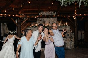 Joyful wedding guests dancing and celebrating inside a rustic venue with string lights and stone fireplace.