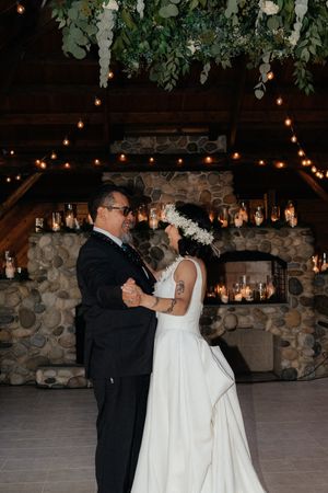 Couple shares first dance in rustic barn venue with stone fireplace and string lights.