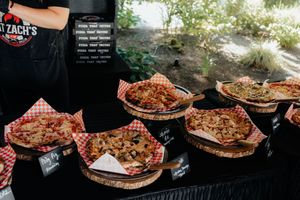 Variety of gourmet pizzas displayed on wooden boards at an outdoor wedding catering station.