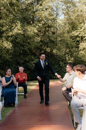 Groom walking down outdoor wedding aisle greeting guests on a sunny day.