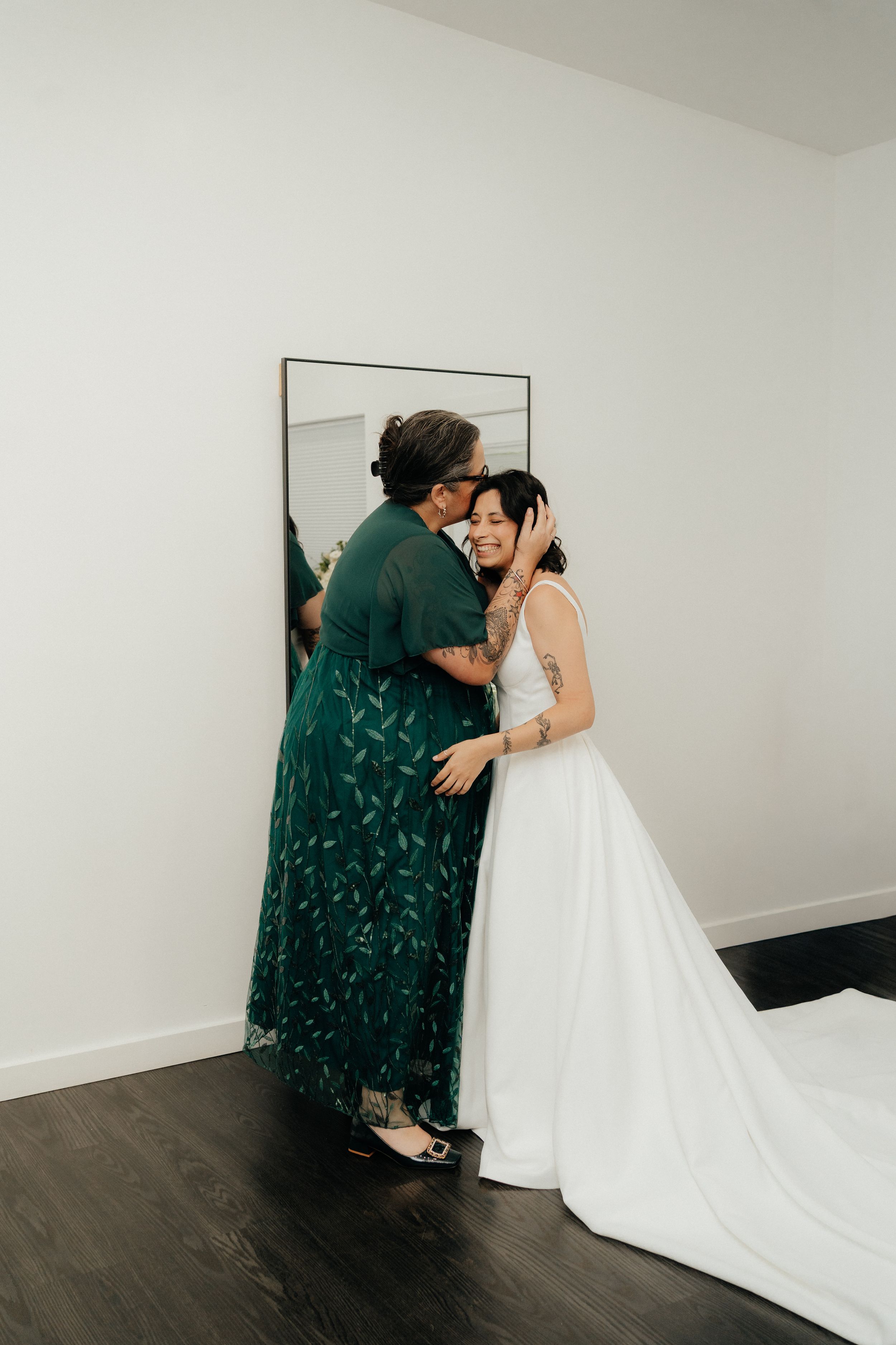 Mother kissing bride on cheek in tender moment before wedding ceremony.
