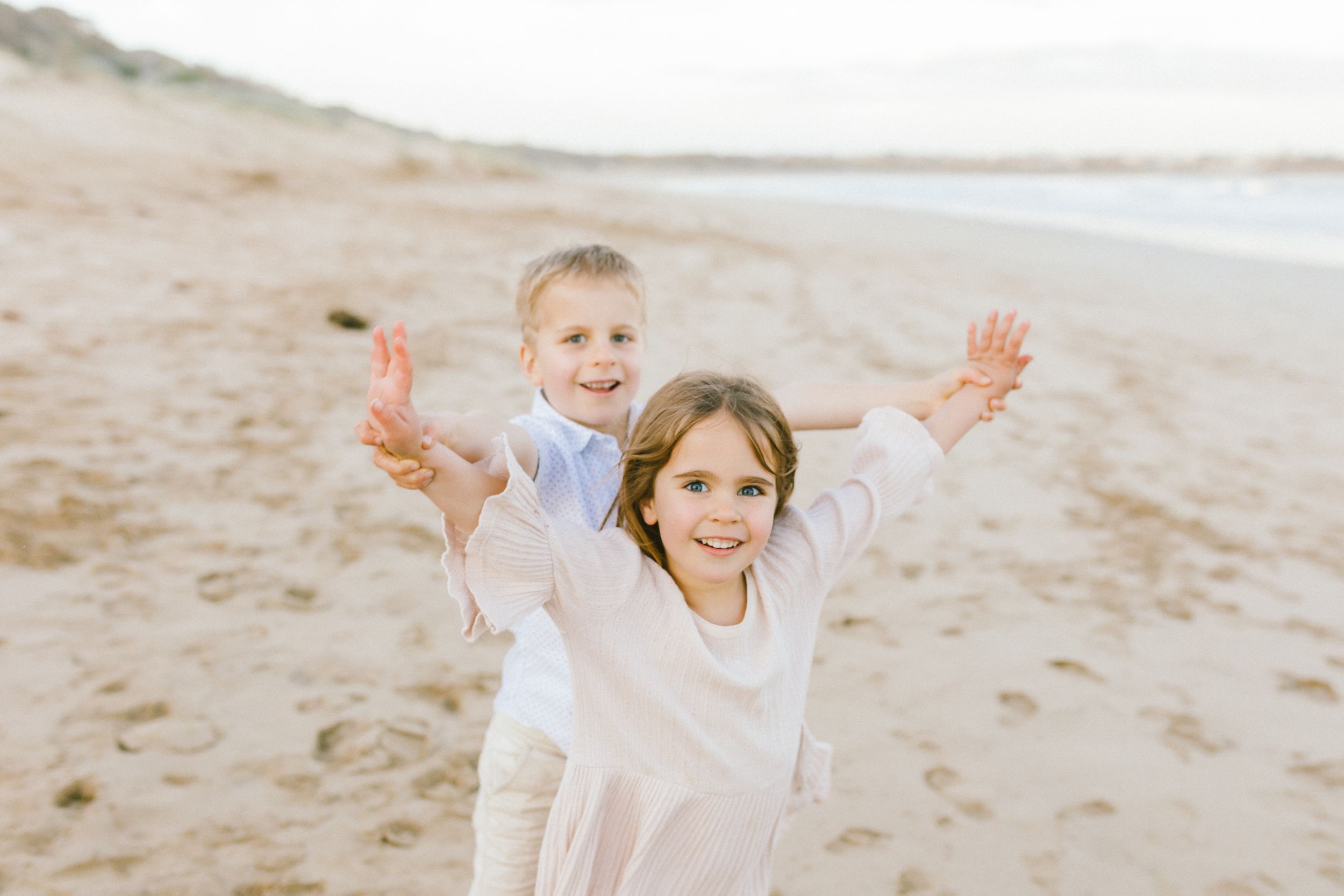 A joyful scene at the beach with people wearing white clothing playing and laughing in the sand.