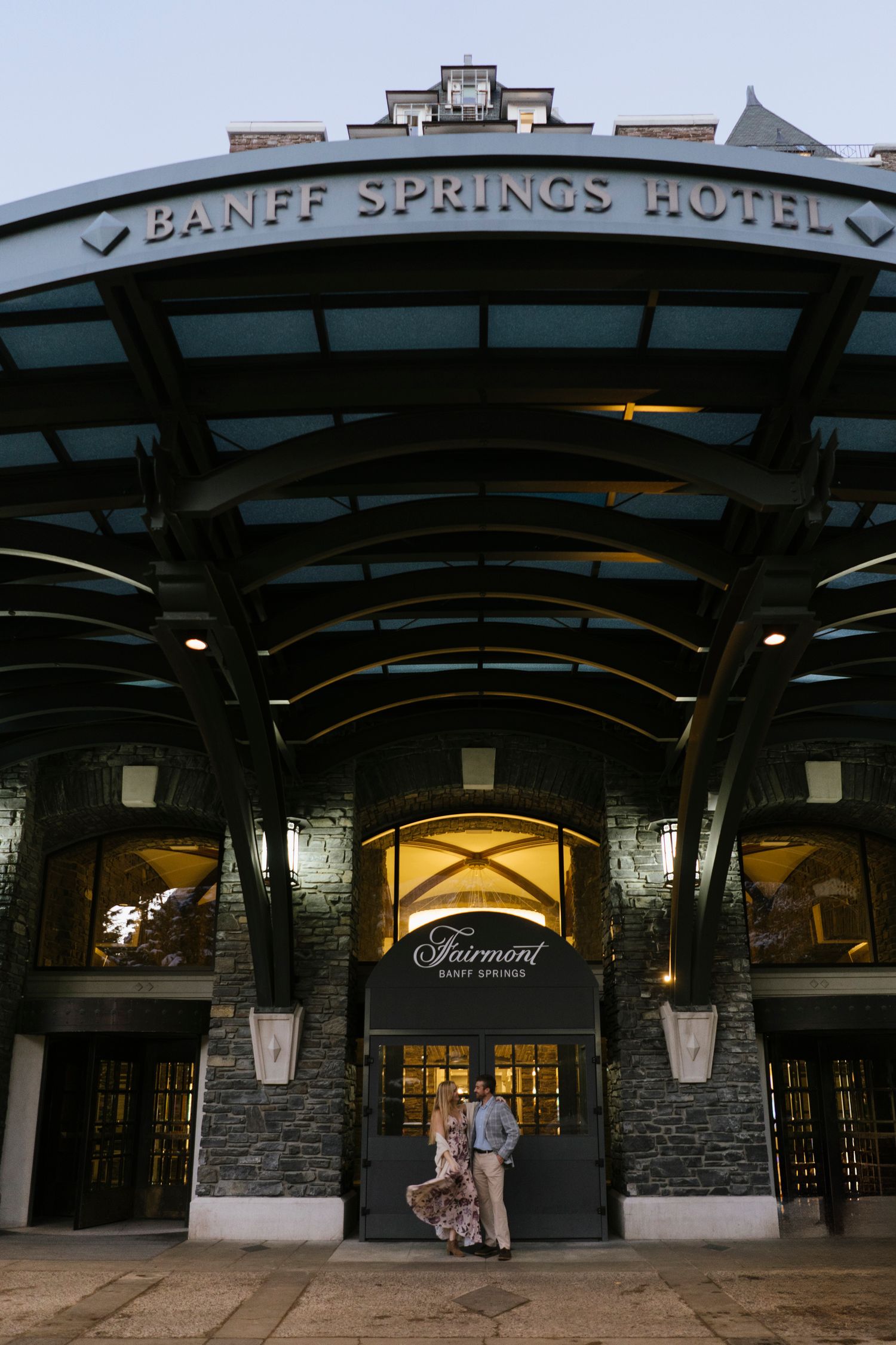 Exterior entrance of the historic Banff Springs Hotel at dusk with illuminated stone archways and signage.