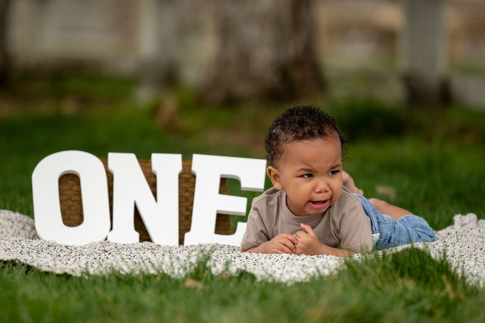A young child lying on white fabric next to decorative 'ONE' letters outdoors.