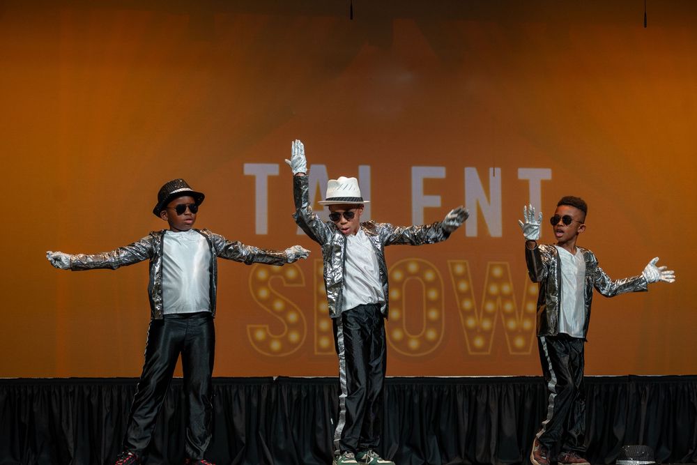 Three performers in matching outfits pose on stage with 'TALENT' text in the background.