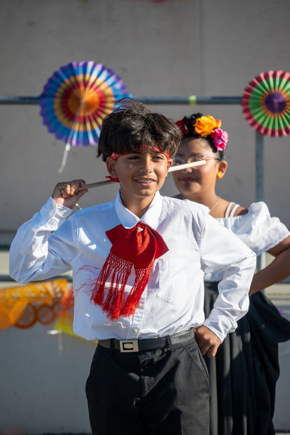 Performers in traditional Mexican folk attire with colorful paper decorations in the background.