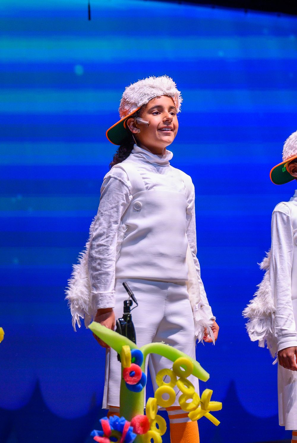 Person in white lab coat costume performs with colorful props against blue background.