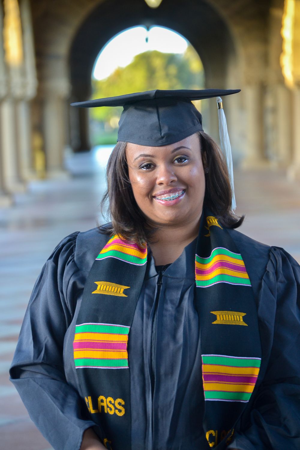 Graduate wearing traditional cap and gown with colorful kente stole celebrates achievement.
