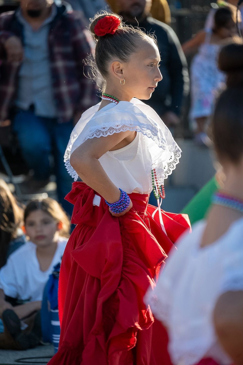 A dancer in traditional Mexican folk costume with white blouse and red skirt performs at a cultural festival.