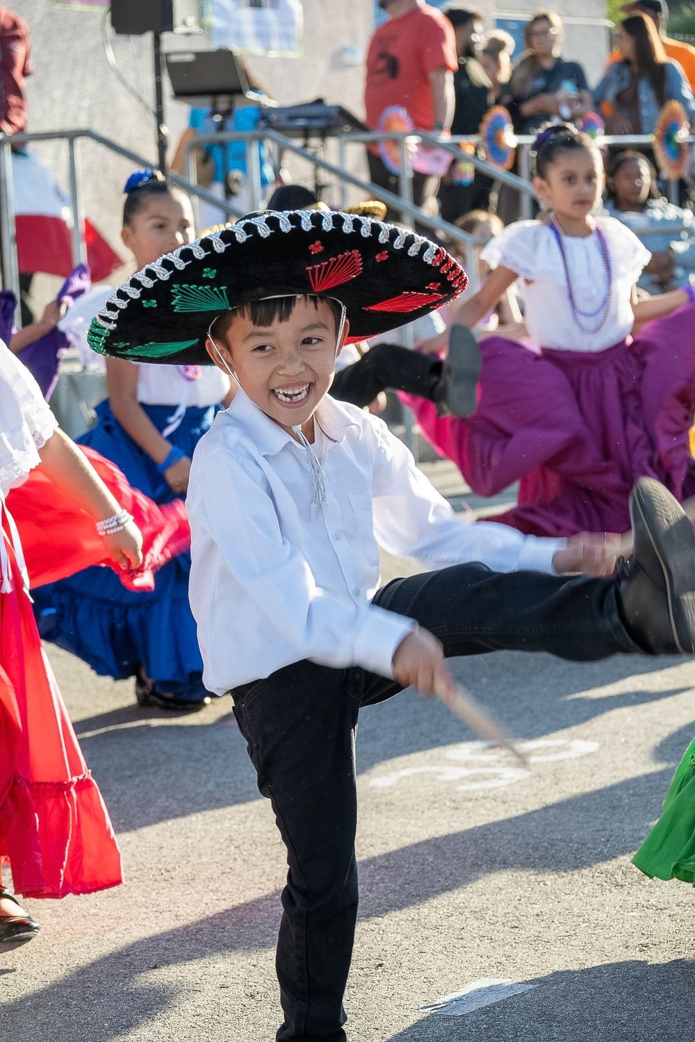 Young dancer performs traditional Mexican dance wearing black sombrero and white shirt.