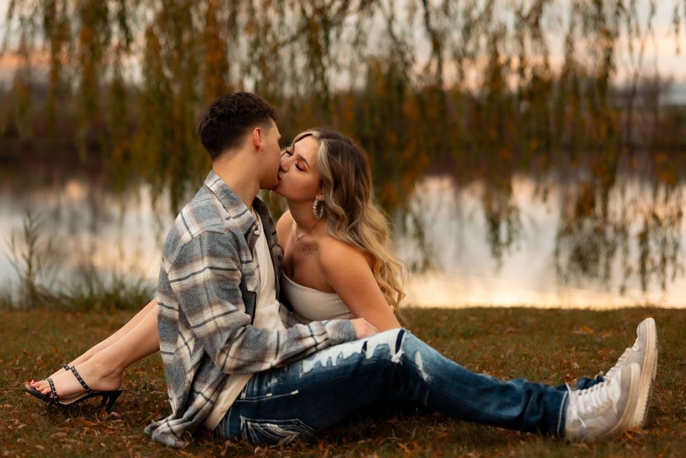 Romantic couple sitting by a lake at sunset with a plaid flannel shirt and jeans creating an intimate moment.