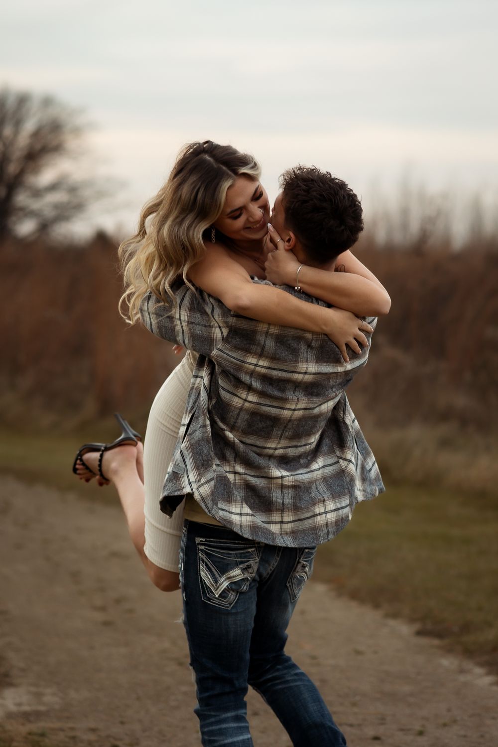 Couple in plaid and denim share joyful spinning moments outdoors at sunset.