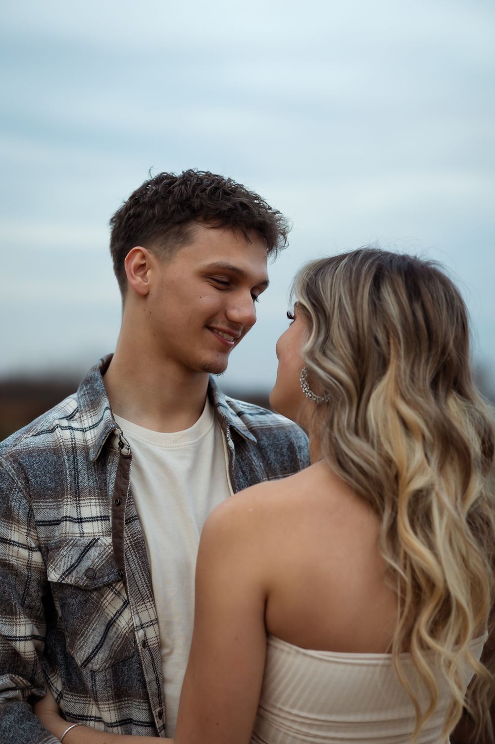 A couple in casual clothing shares tender moments against a light blue sky background.