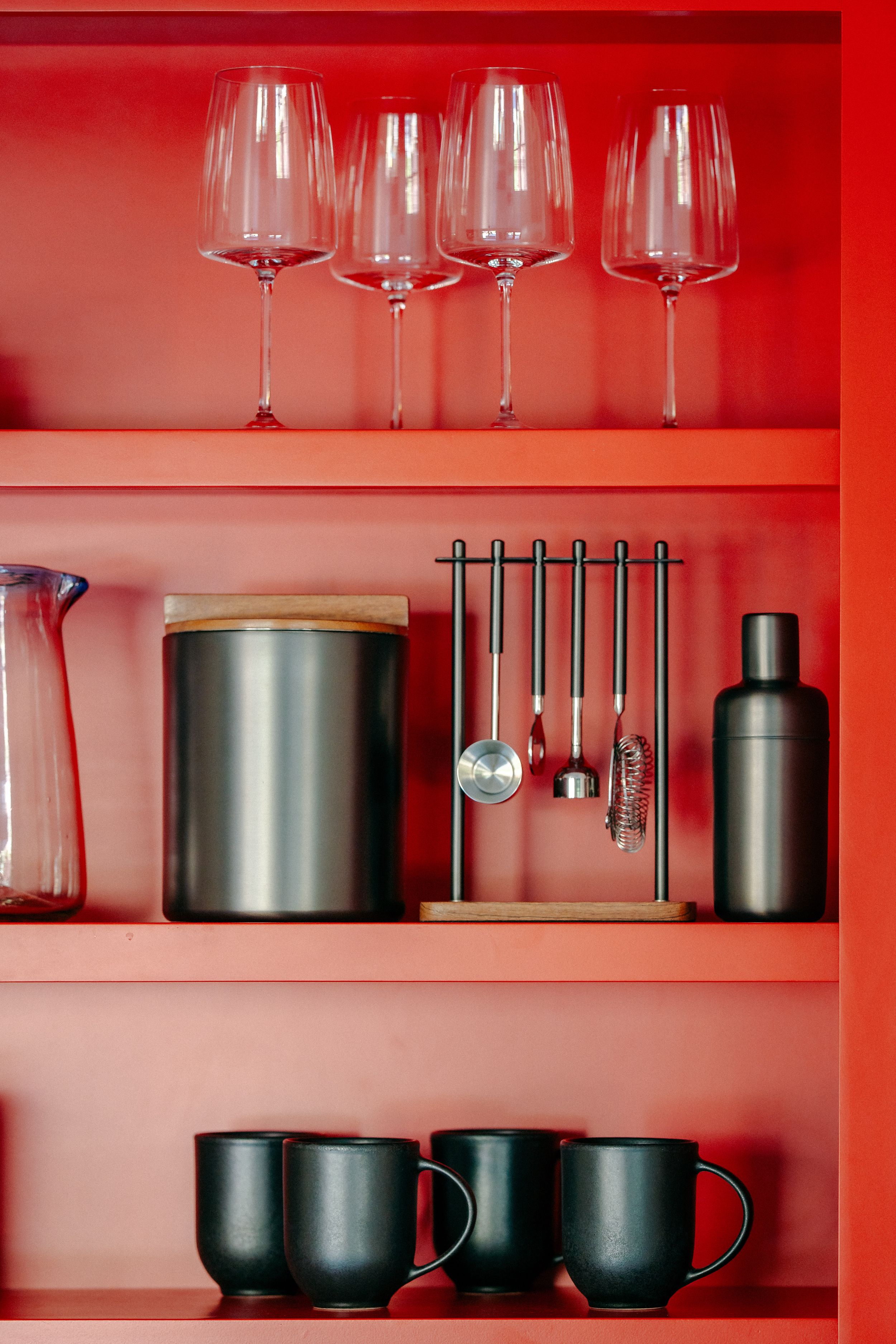 Modern kitchen shelving with wine glasses and metallic kitchenware arranged against a vibrant red wall.