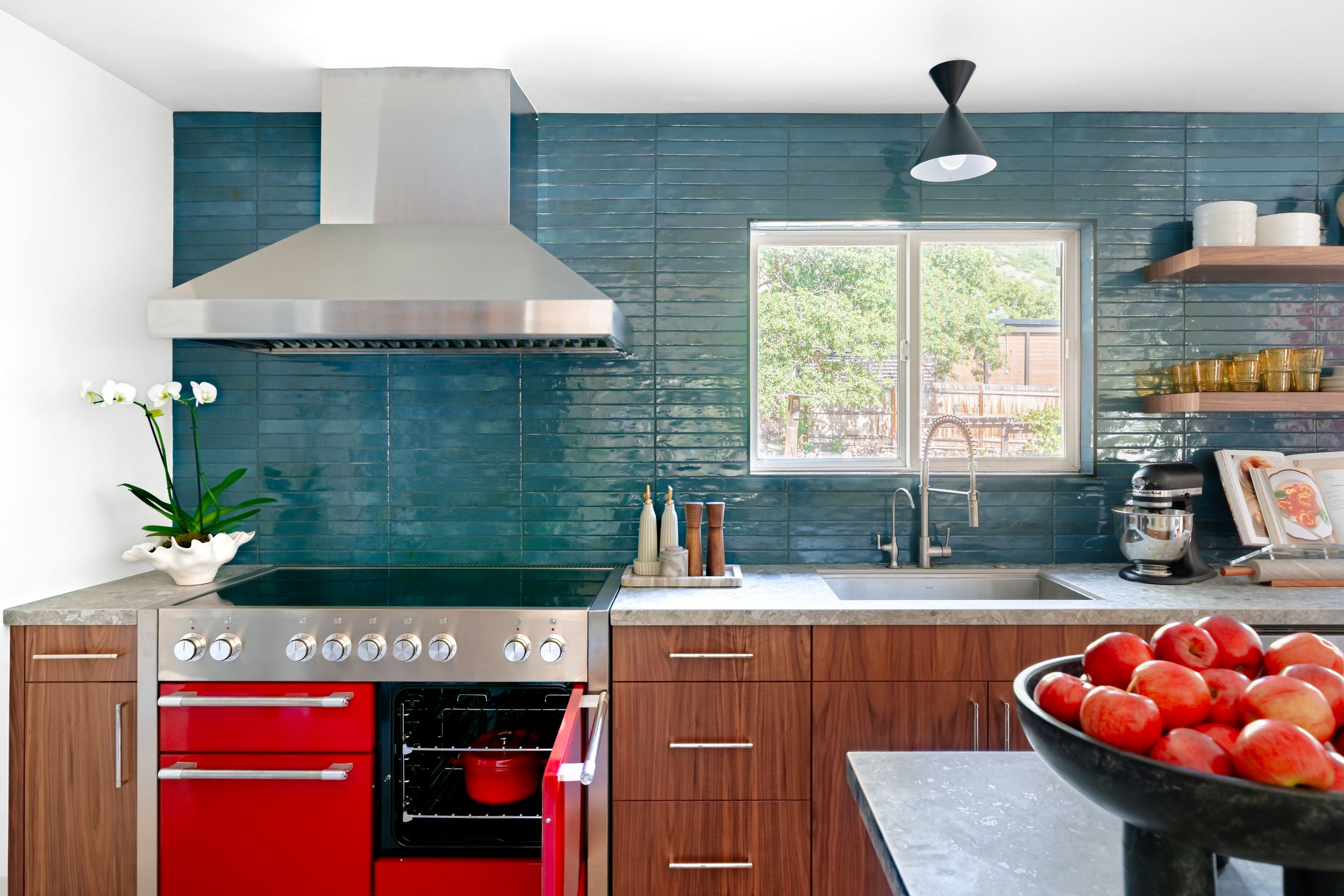 Modern kitchen features teal subway tile backsplash, wood cabinets, and stainless steel appliances.