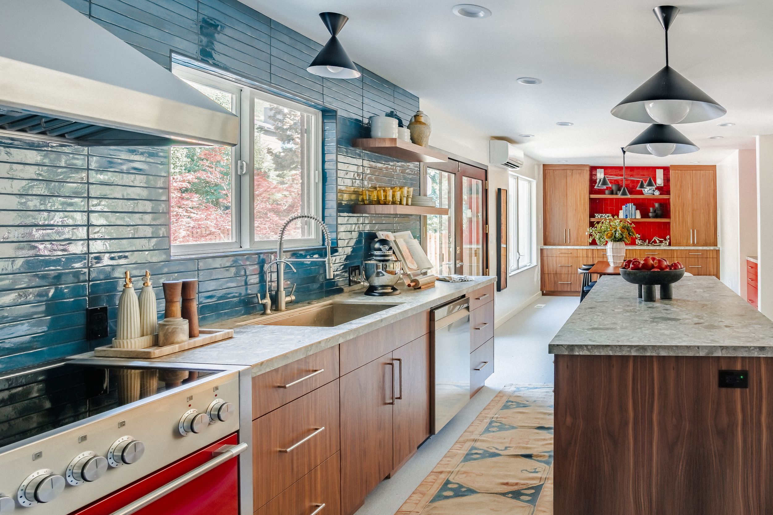Modern kitchen interior with wood cabinets, stainless steel appliances, and blue tile backsplash features sleek pendant lighting.