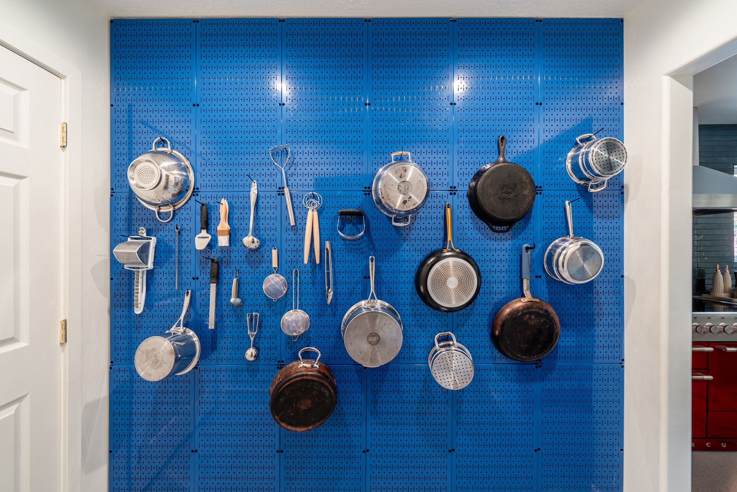 Shiny pots and pans hang from hooks against a bright blue tiled wall in a professional kitchen.