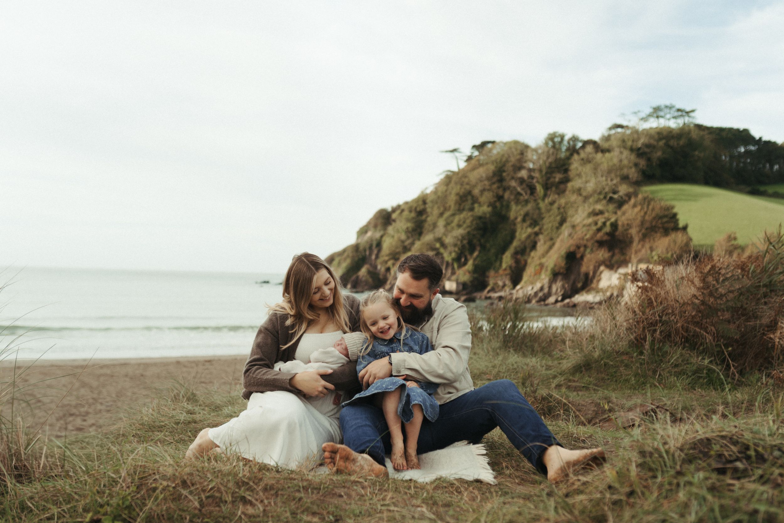 A couple embraces on a scenic coastal cliff overlooking the ocean during sunset.