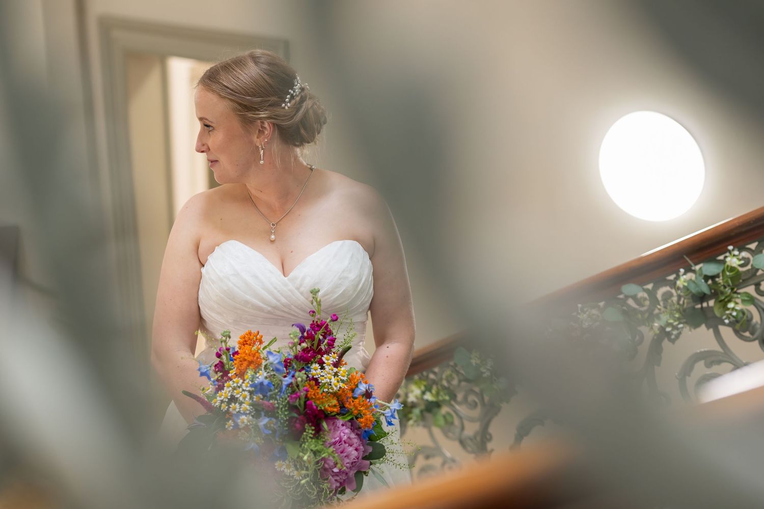 A bride in a white strapless wedding dress holds a vibrant bouquet of orange, purple and blue wildflowers.