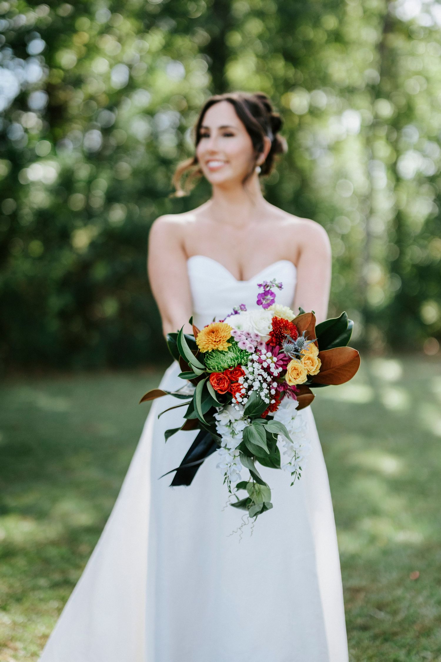 A stunning bridal bouquet with vibrant orange, red and purple flowers against a white wedding dress in a garden setting.