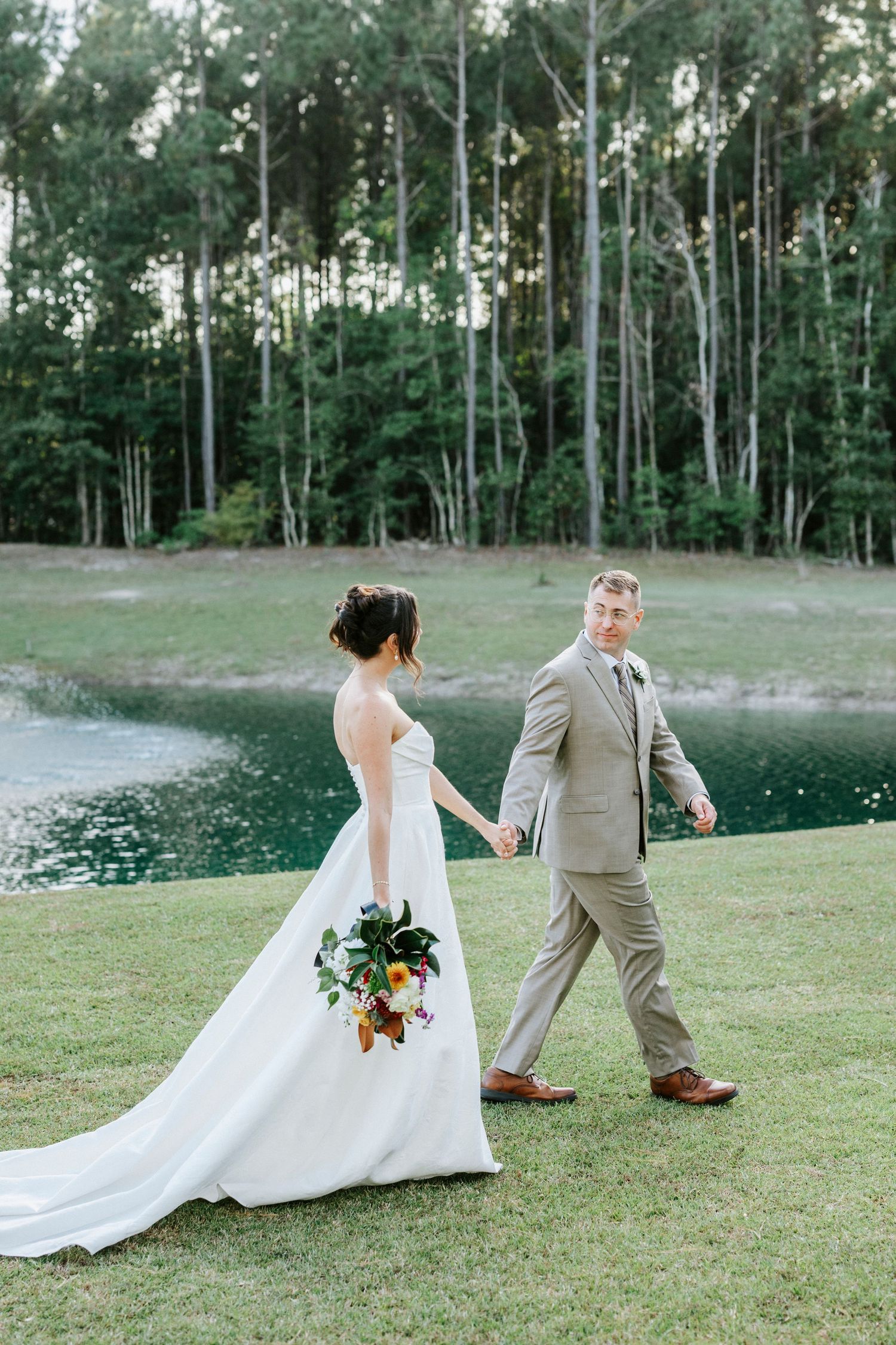 A playful wedding photoshoot on grassy slopes with tall trees in the background.