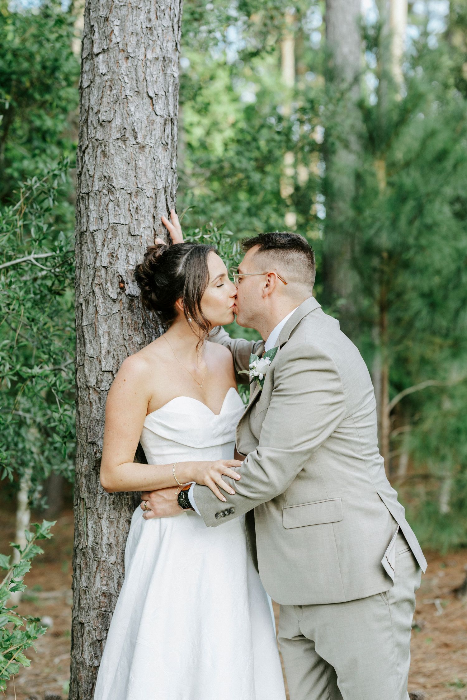 A romantic moment captured between newlyweds in a wooded setting with sunlight filtering through the trees.