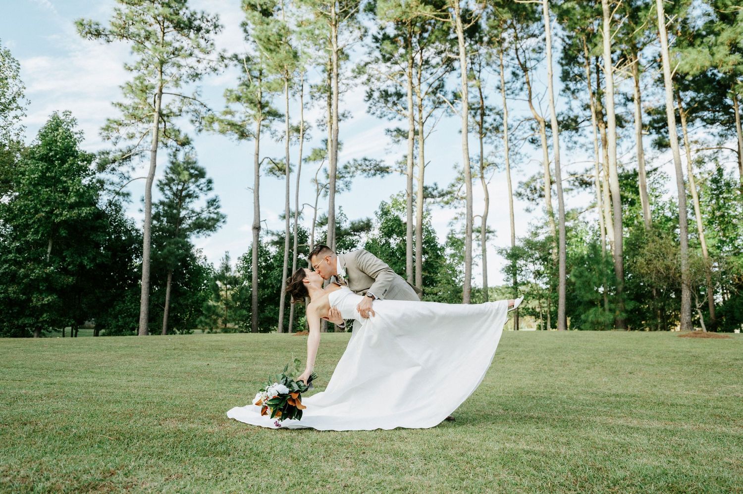 A white veil blows gracefully in the wind against a backdrop of tall pine trees and green grass.