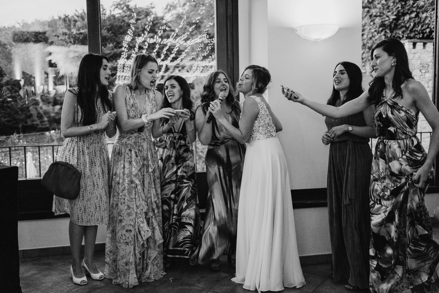 Black and white photo of bride laughing with group of women in elegant dresses at a wedding reception.