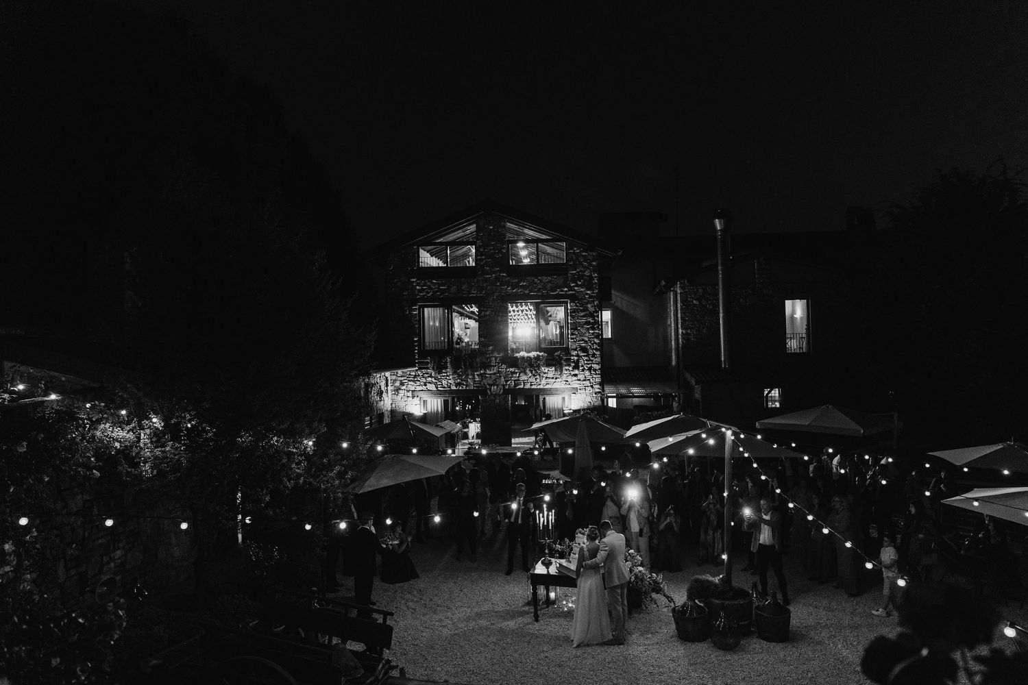 Black and white aerial view of a romantic outdoor wedding reception with string lights at night.