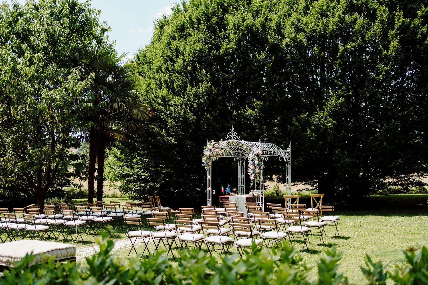 Outdoor wedding ceremony venue with white gazebo altar and rows of wooden chairs on green lawn.