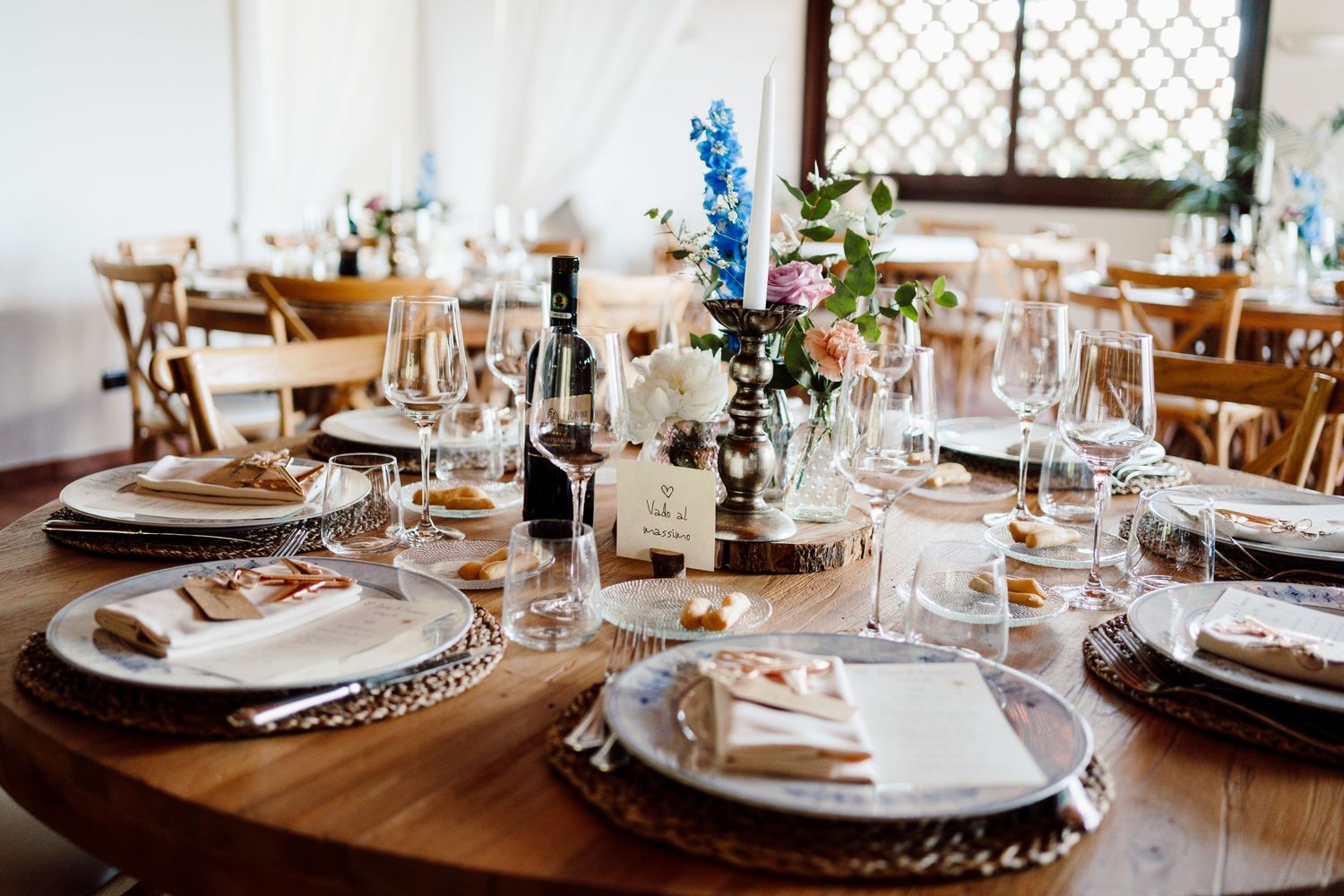 Elegant wedding reception table set with glassware, floral centerpieces, and a wine bottle.