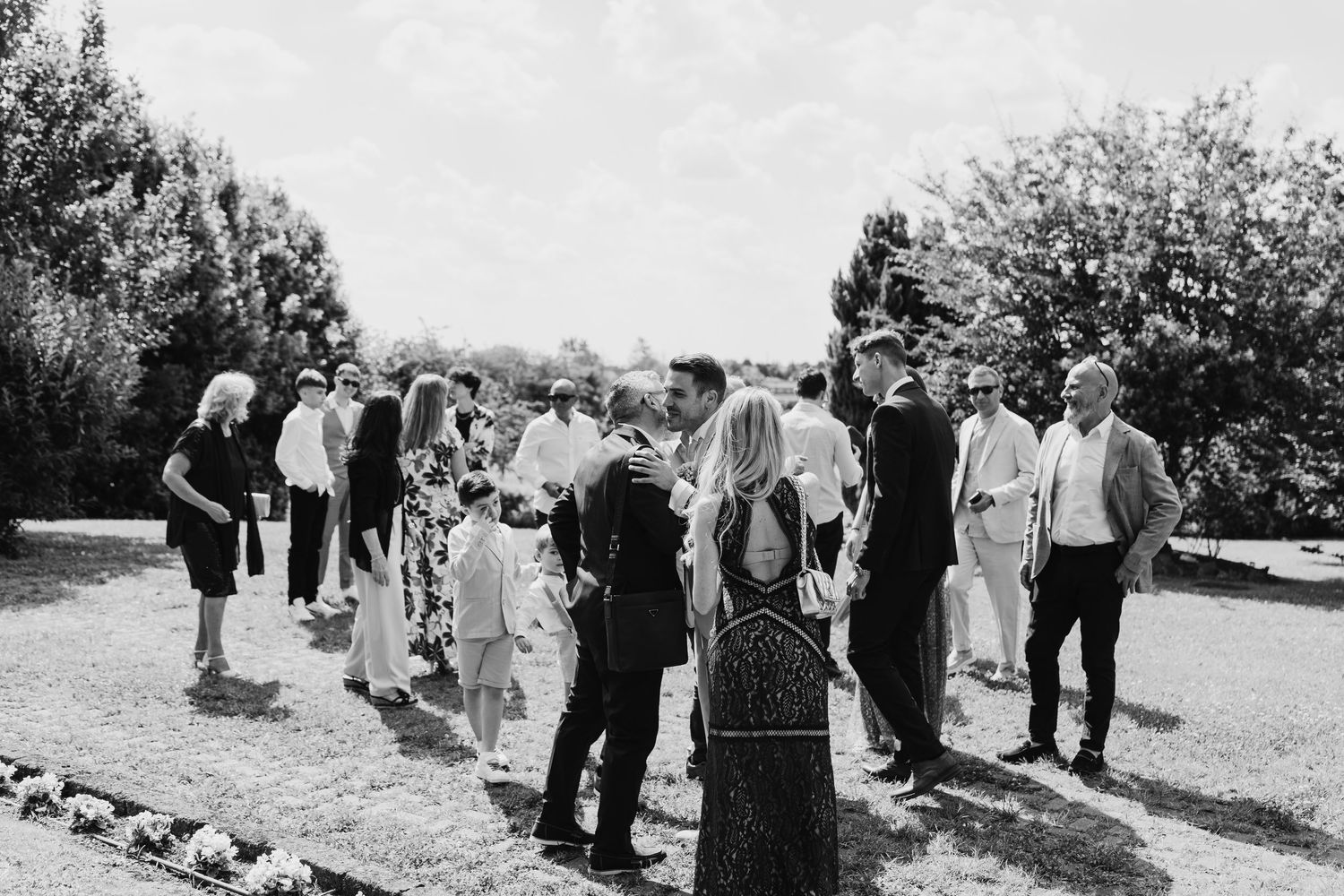 Black and white photo of wedding guests mingling outdoors on a sunny day.