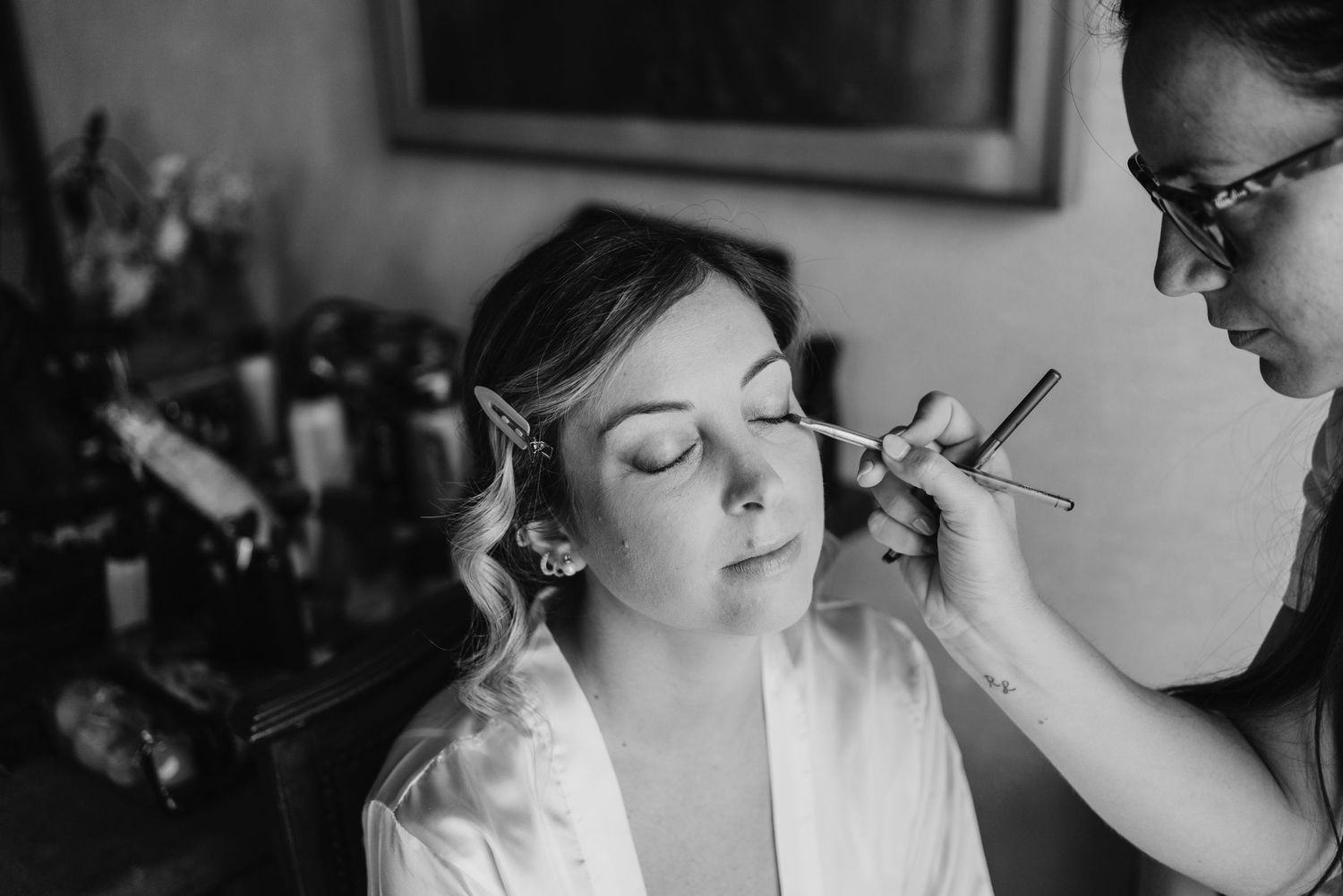 Black and white close-up of a makeup artist applying eyeshadow to the bride.