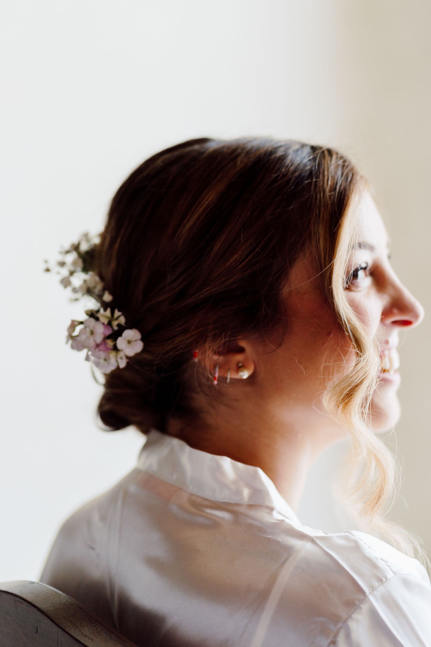 Elegant bride with floral hair accessory and pearl earrings smiling softly in profile view.