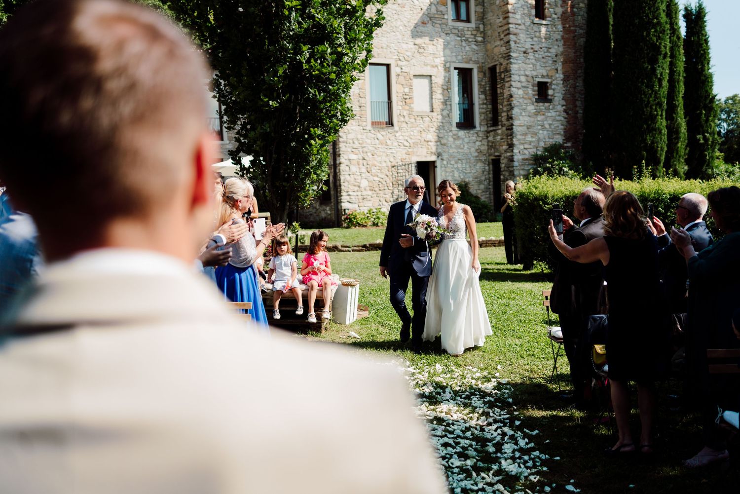 Bride and groom walking down aisle at outdoor garden wedding ceremony with guests applauding.