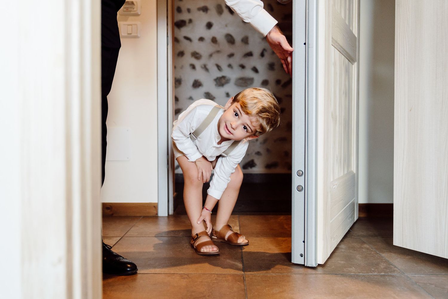Adorable young boy in white shirt peeking through doorway at wedding venue.