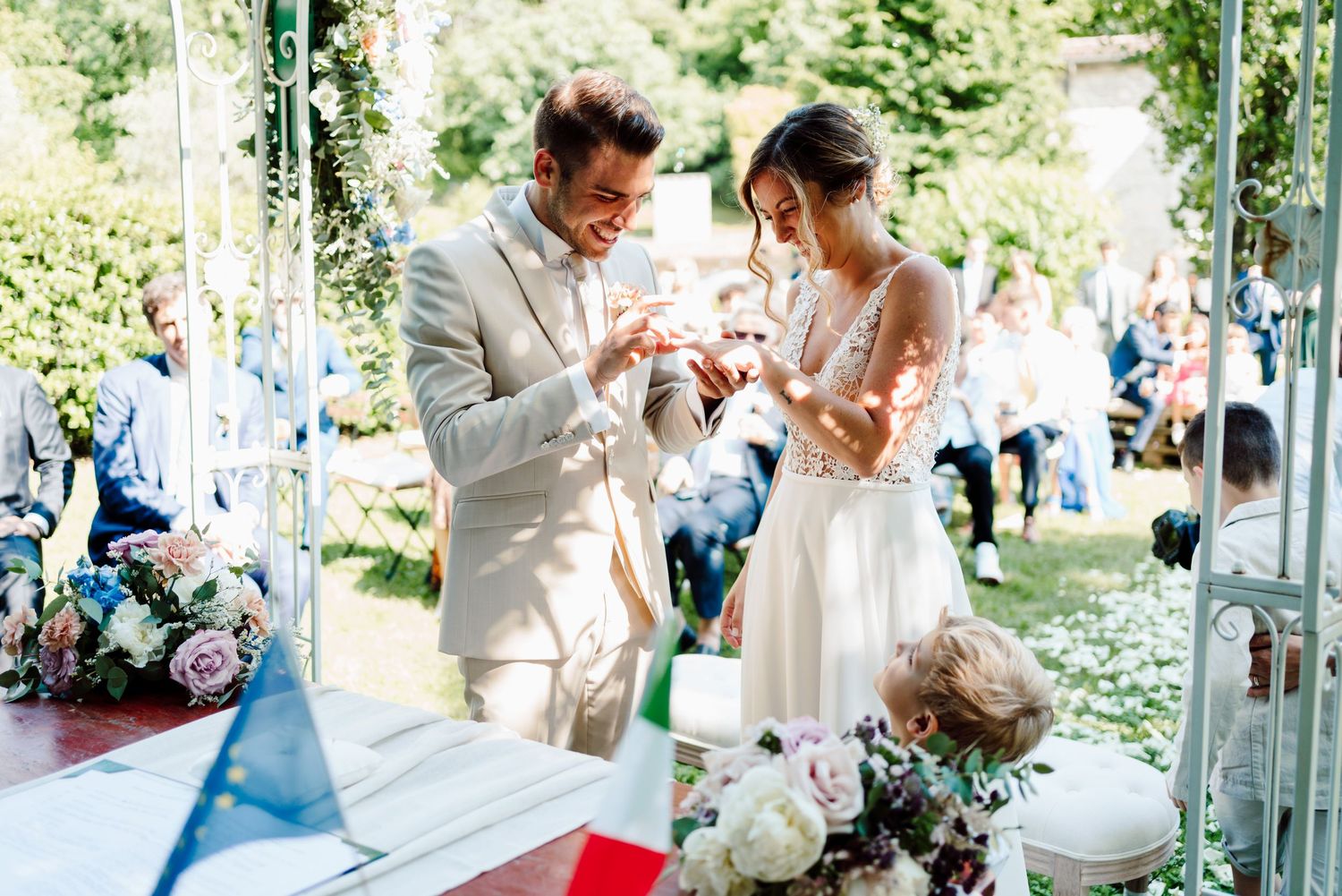 Bride and groom exchange wedding rings during an outdoor garden ceremony with floral decorations.