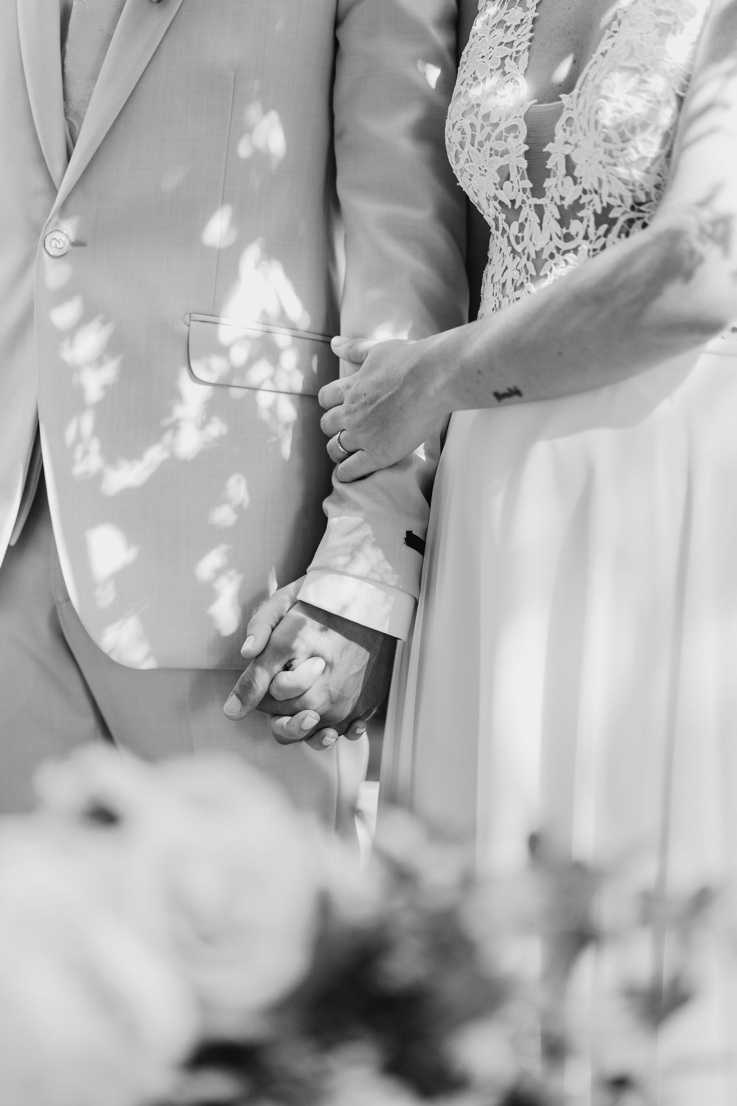 Black and white photo of bride and groom holding hands during their wedding ceremony.