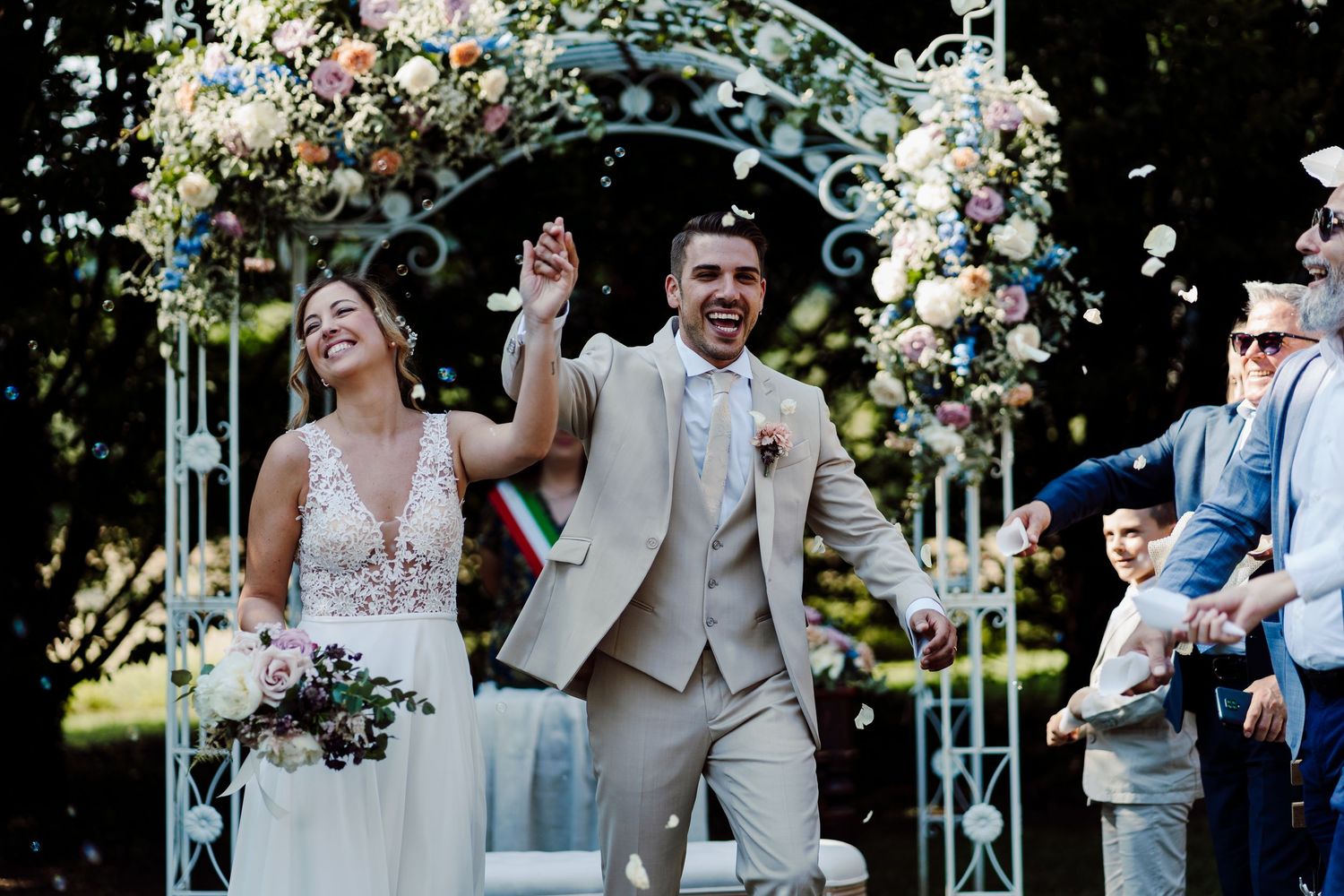 Joyful bride and groom celebrate walking back down the aisle under a floral wedding arch.
