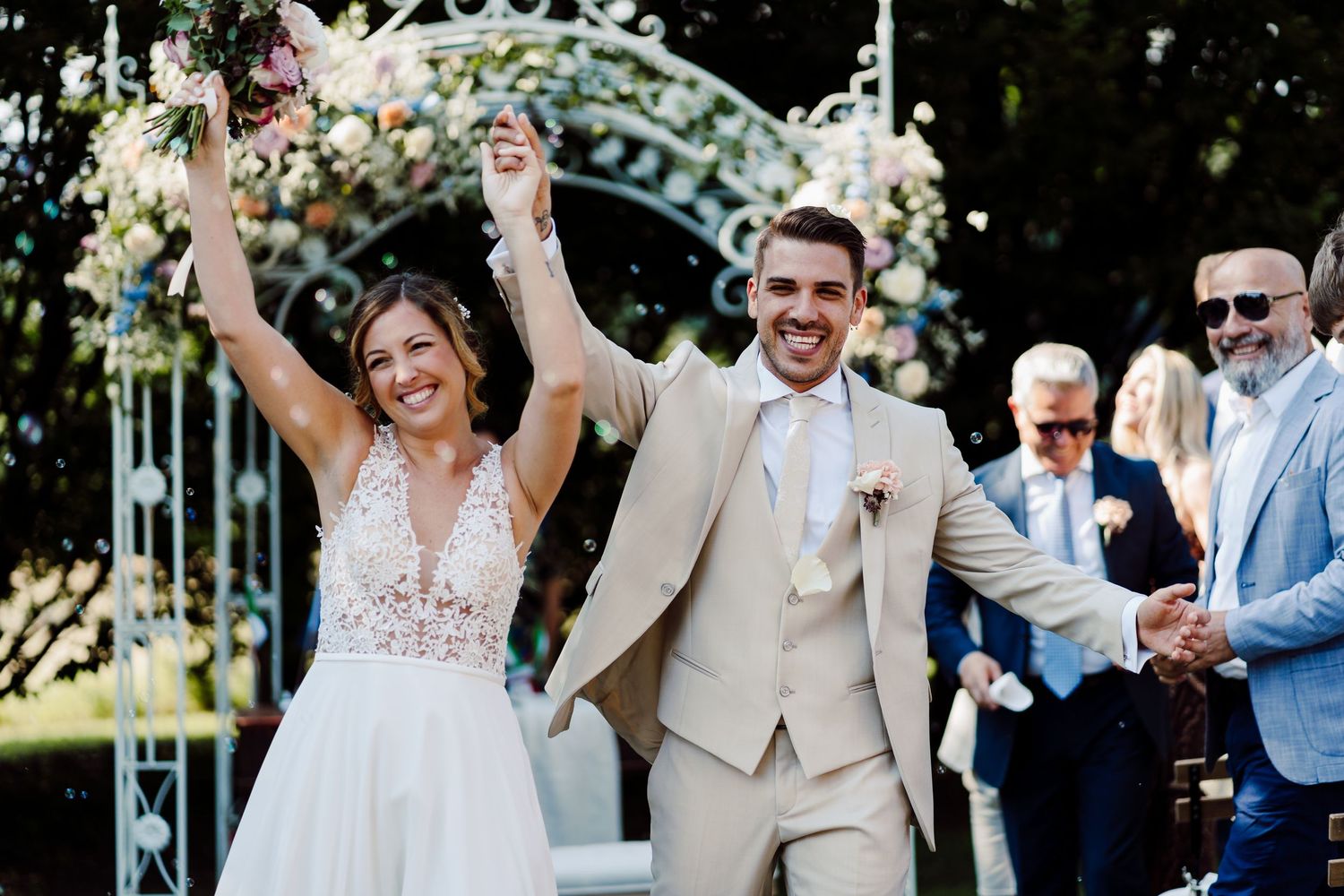 Excited bride and groom raise their arms in celebration after their outdoor garden wedding.