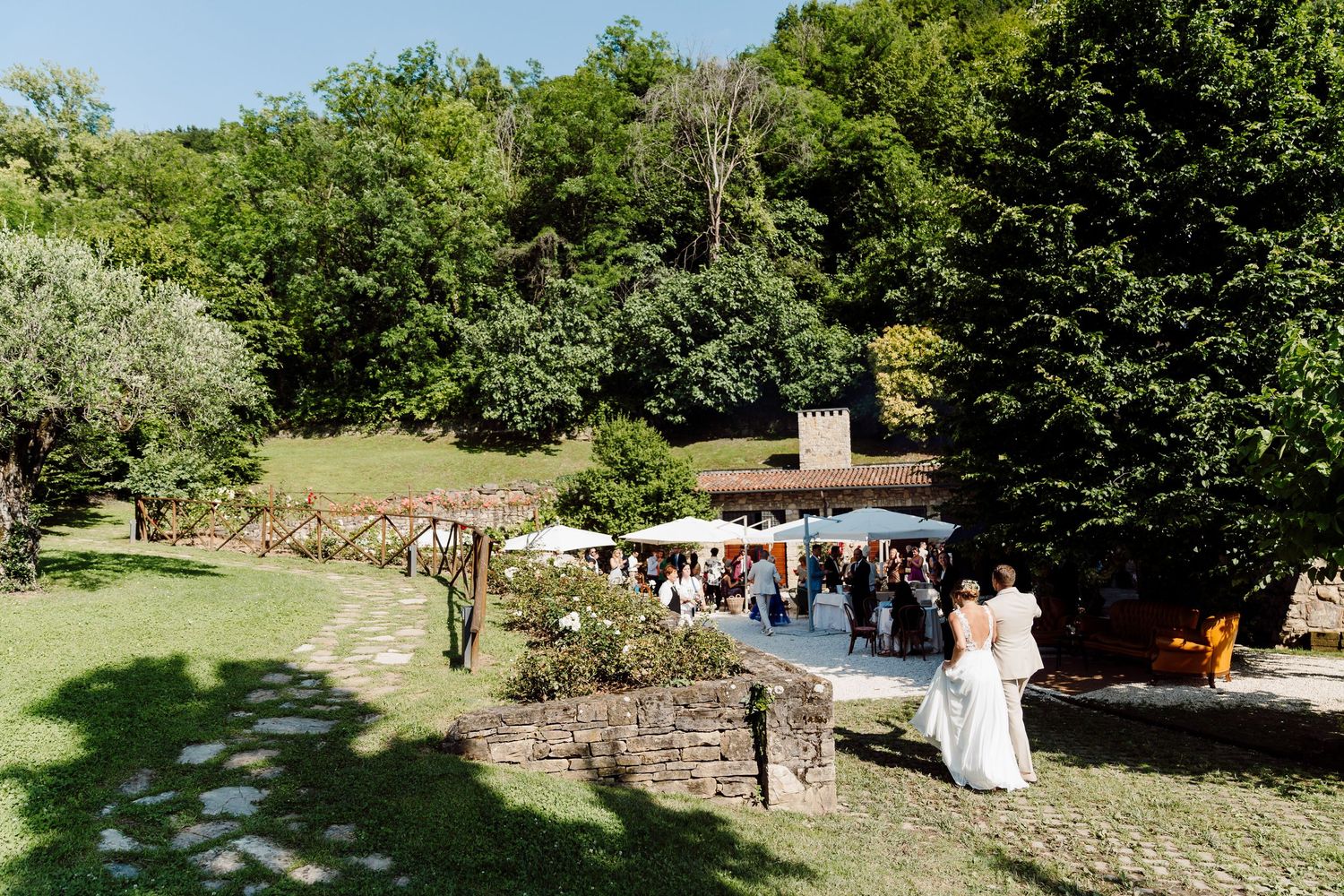 Aerial view of elegant outdoor wedding reception with guests mingling on stone terrace surrounded by lush greenery.